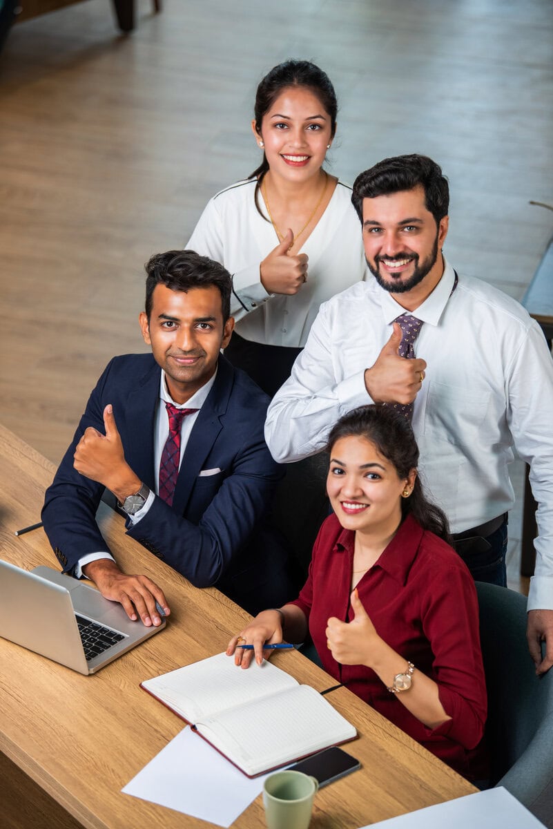 Young Indian asian leader coach teaching employees group analyzing online project explaining business strategy speaking training diverse corporate team with laptop using computer at office meeting